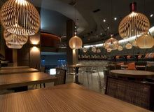 Moderne Restaurantbeleuchtung mit hölzernen Pendelleuchten über Holztischen.