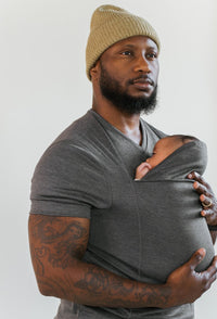 Mann mit grauem T-Shirt und Baby in Tragetuch, Mütze, tätowierter Arm, Familienmode.